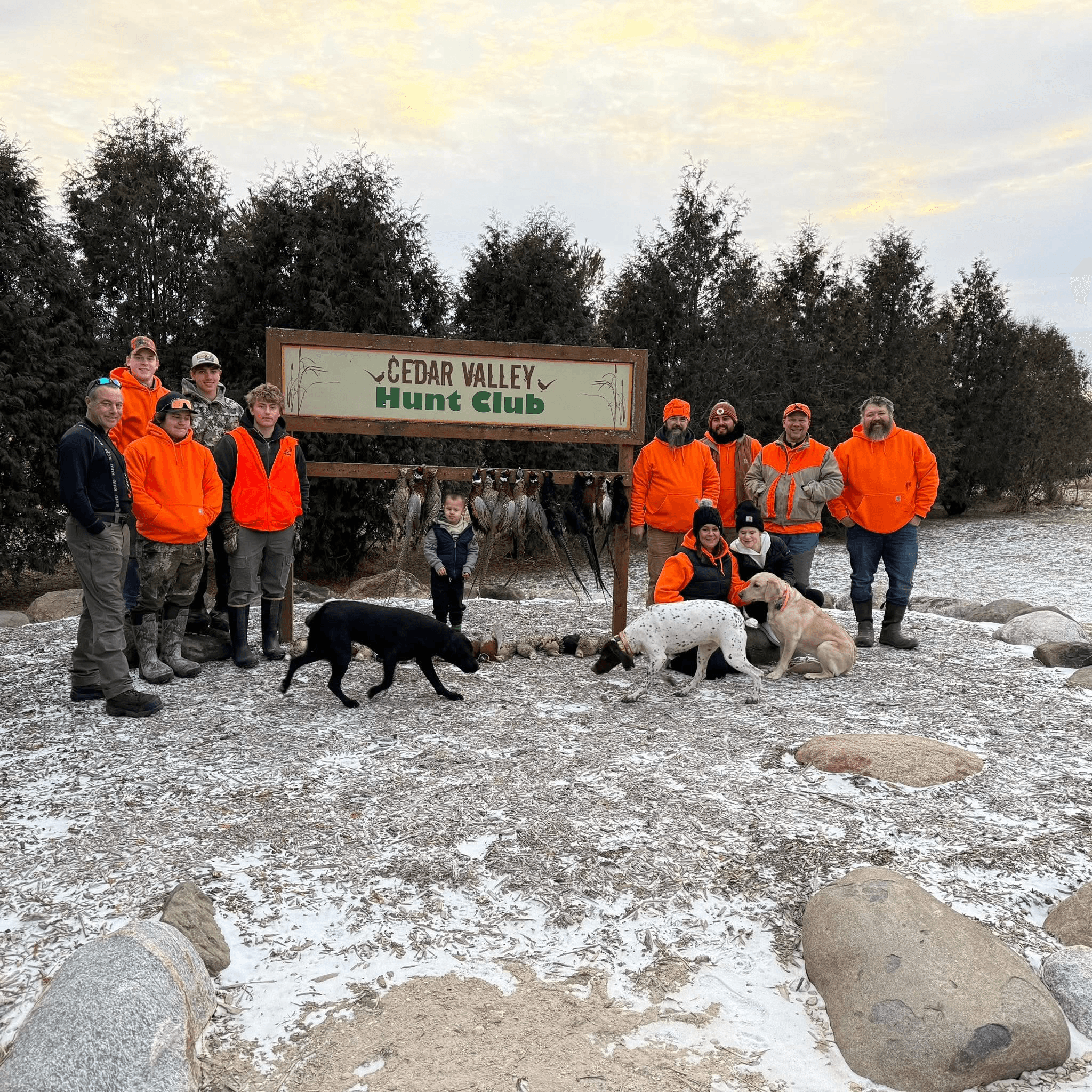 Greatland Electric team in blaze orange with hunting dogs at the Cedar Valley Hunt Club sign