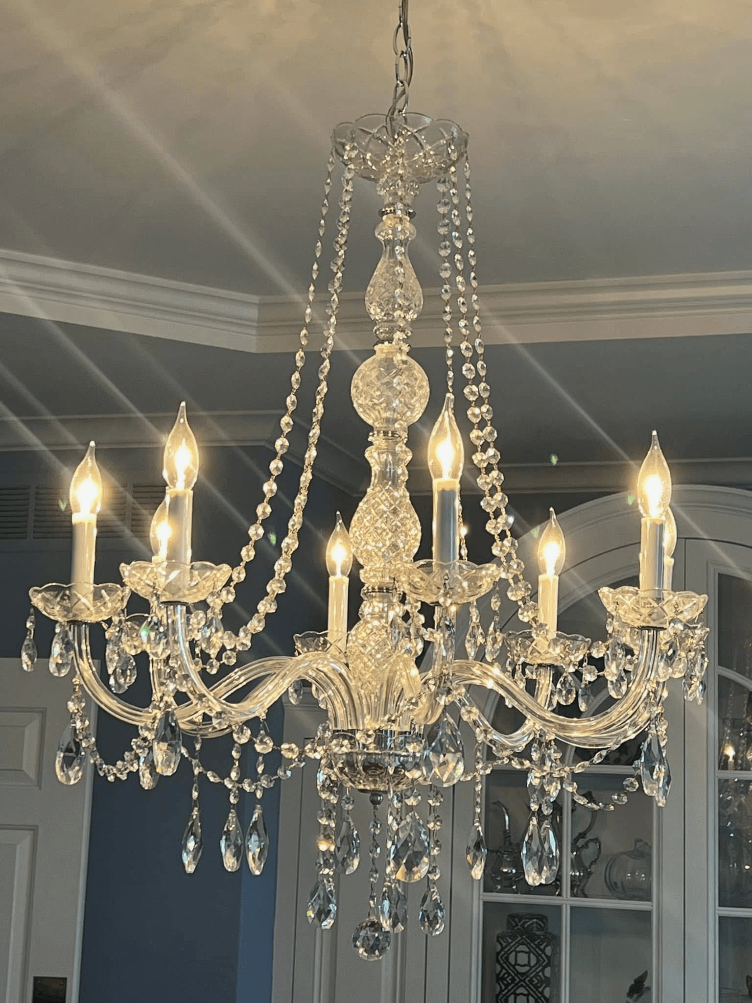 Crystal chandelier with candle-style bulbs installed in a blue dining room with white crown molding
