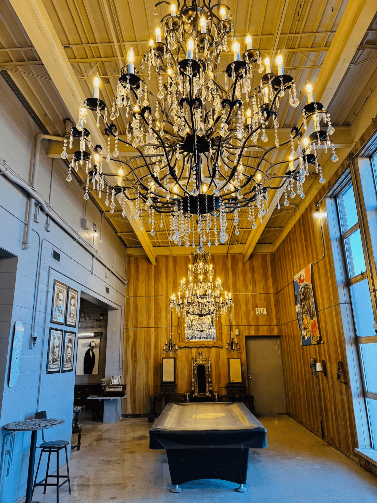 Oversized black iron and crystal chandelier hung from a tall wood-paneled ceiling above a pool table